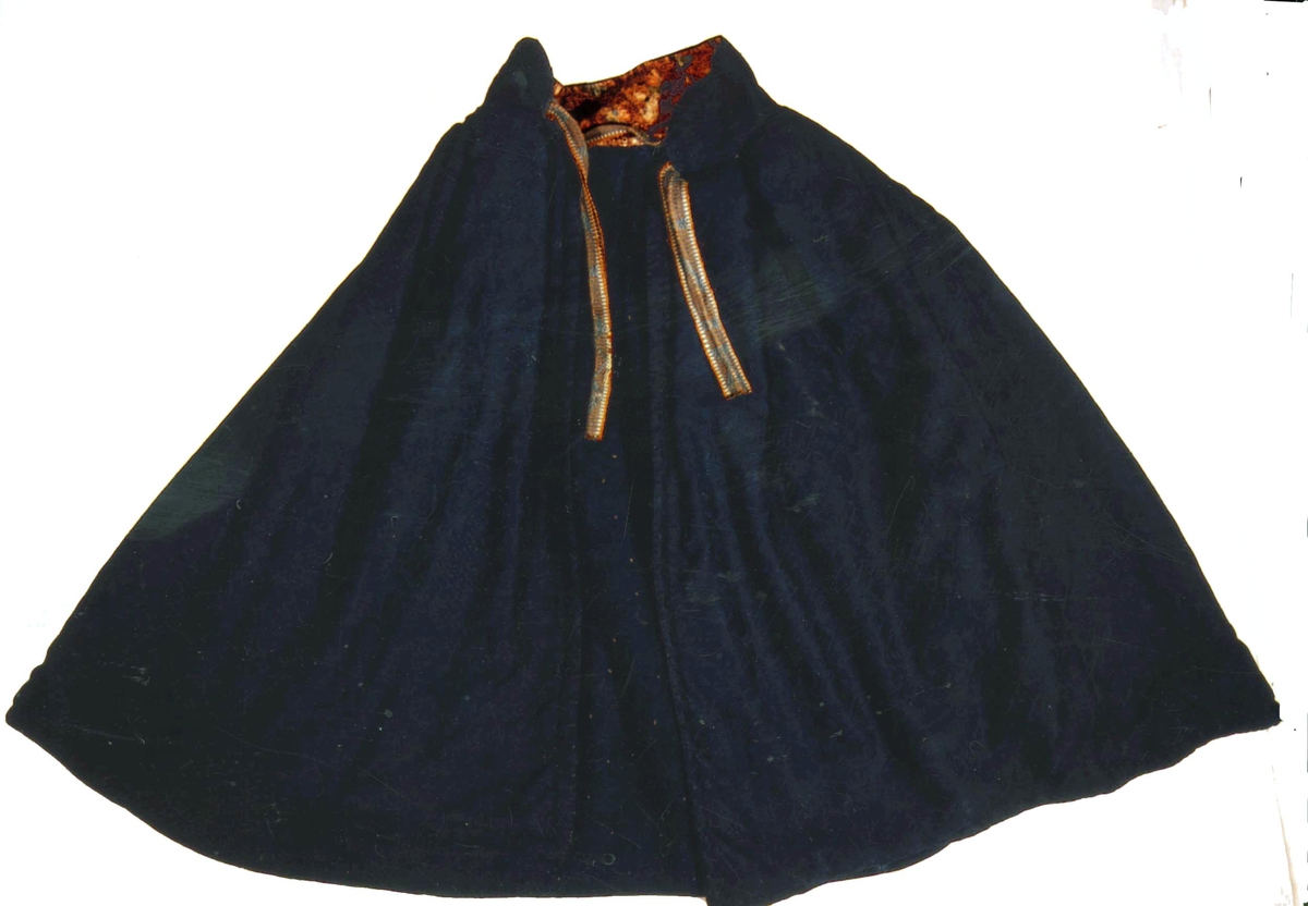 Mørk blå kep. Ytterstoff i everlasting. Fôr i hjemmevevet ullstoff i kypert. Halslinning er fôret med kattun (mørk brunt med blomster i rosa/blått). Kepen lukkes med ripsvevd knytebånd i halsen. 