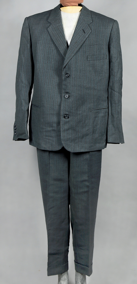 Dress med gråstripete mønster i stoffet, enkelt spennet jakke som kneppes med tre knapper. Jakka er silkefôret, unntatt ermene. Bukse med fire lommer. 