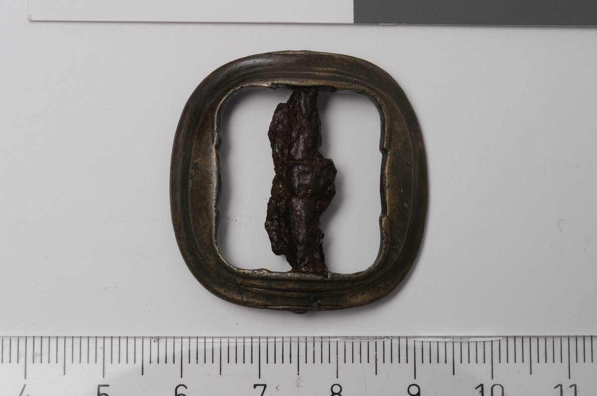 MALV: 33, 2*33, 2 MM. RAMMENS B. 7 MM, STØPT TILNÆRMET KVADRATISK SPENNE. HJØRNENE ER AVRUNDET. RAMMEN HAR RETTE KANTER PÅ INNSIDEN. MÅ RENSES. OVERSIDEN HAR SVAKE LINJER SOM FØLGER RAMMEKANTEN SOM DEKOR. SPENNEN ER SVAKT BUET: LIGNER I FORM LXXVIII NR. 24 I NORSK BONDESYLV (RIK. BERGE).