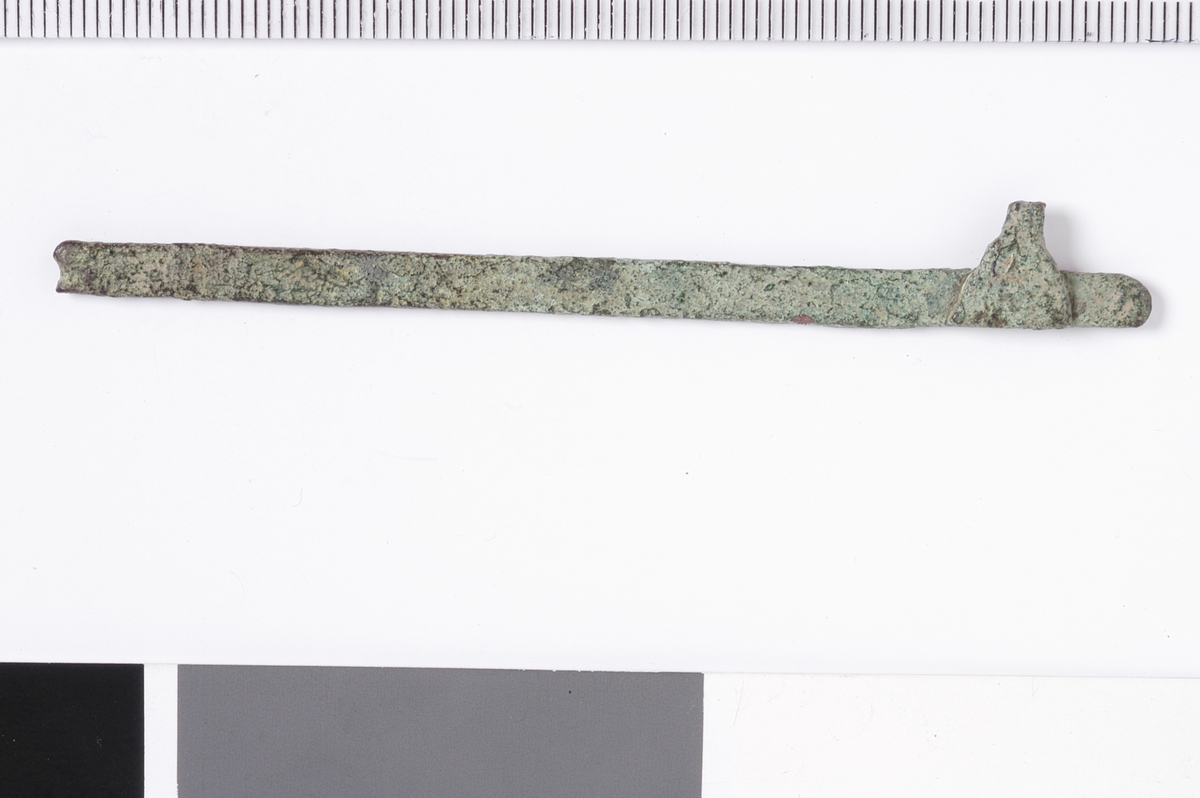 En lang og jevn metallstang med jevn tykkelse og rette, filte kanter som er buet i enden. I motsatt ende sees en bruddflate. Det er ingen tegn til dekor. I den bevarte enden sees et trekantet metallstykke som er festet til metallbjelken, med en avsmalning i nedkant av bjelken. dett ekan være emne til en bjelke til en enkel skålvekt.