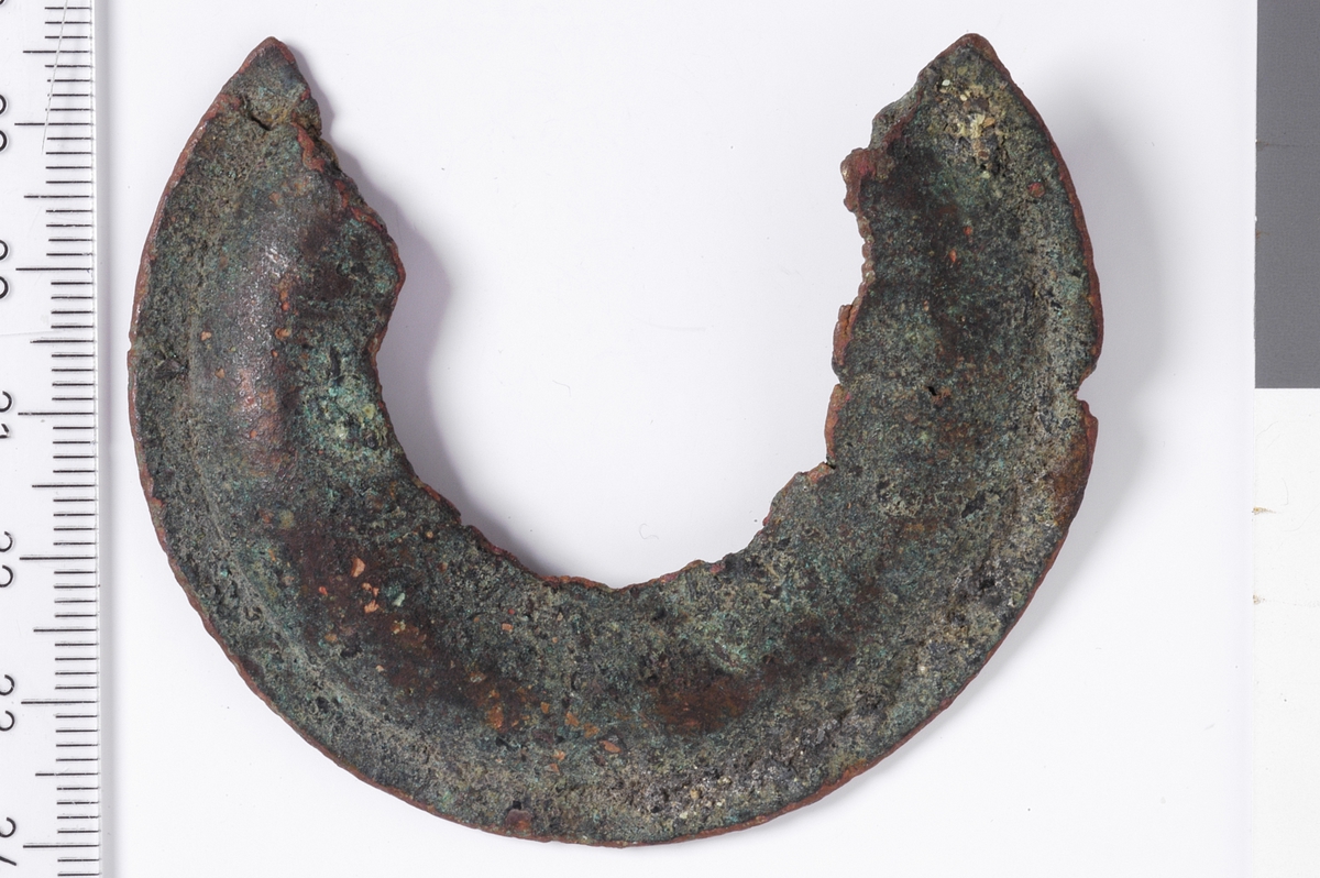 Sirkelformet metallplate med jevn ytterkant og en bruddfalte klangs hele innsiden, samt i begge kortender. det er ingen tegn til dekor, men platen er flat i ytterkant og har deretter en konveks bue som går innover. Dette er et kraftig beslag, men med ukjent bruksområde.