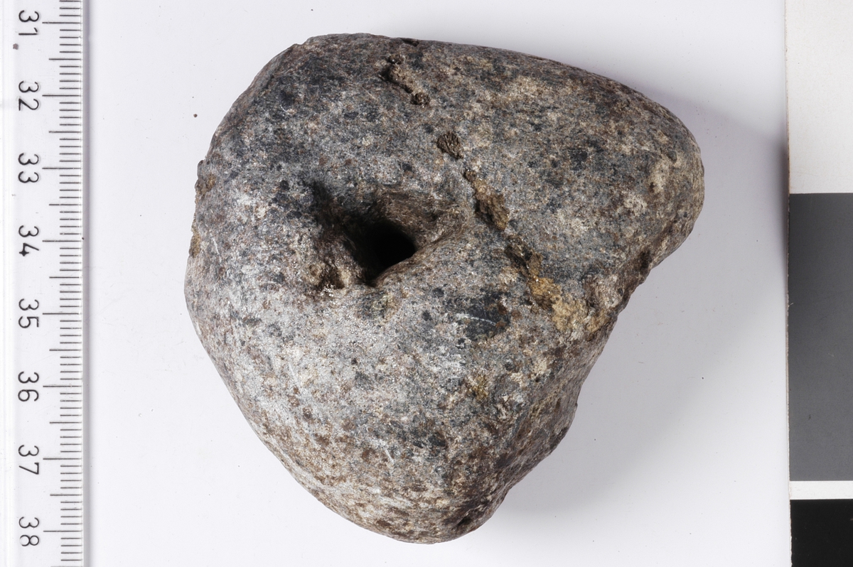 MALV: L. 5, 9 CM, ST. B. 6, 8 CM, T. 3, 4 CM, UREGELMESSIG REKTANGULÆR FORM, SPISS AVRUNDET I DENENE ENDEN HVOR HULLET ER. SLITESPOR ETTER SNØRE I OVERKANT AV HULLET. 