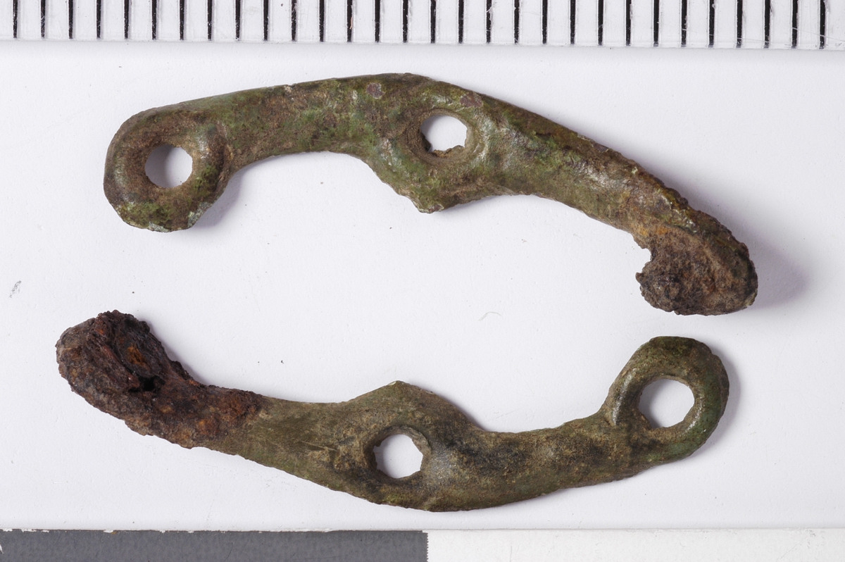 MÅL: L. (BEGGE) 2, 4 CM, TO BØYLER AV KOBBERBLIKK, DREVET UT FRA BAKSIDEN. HVER BØYLE HAR TRE HULL. GJENNNOM DET ENE HULLET GÅR EN JERNNAGLE SOM OPPR. HOLDT DE TO STYKKENE SAMMEN.