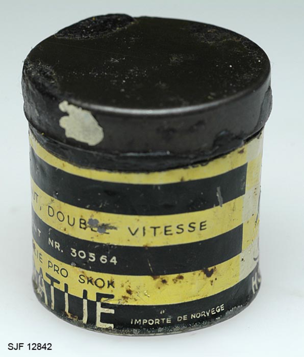 Boksen med skismurning har sylindrisk form. Den består av en metallsylinder og et lokk. Utenpå metallsylinderen er det påklistret en etikett hvor det bl. a er bilde av en skihopper som utfører et svev (øvrig informasjon fra etiketten er ført inn i feltet for påført tekst). 
Teksten som er påskrevet øverset på boksen er nesten helt borte, slik at det er umulig å tyde hva som har stått der. Etter hvert som man har brukt smurning, har det vært nødverndig å rive av deler av boksen, og dermed har deler av den påførte teksten på boksen fulgt med. 