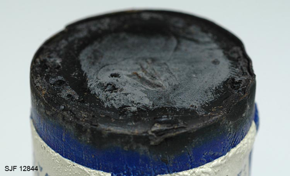 Boksen med skismurning har sylindrisk form. Den består av en metallsylinder med en papphylse utenpå og et lokk. Utenpå metallsylinderens papphylse er det bilde av en skiløper.  Oppå lokket er det avbildet en skiløper nærmest som et relieff. 
