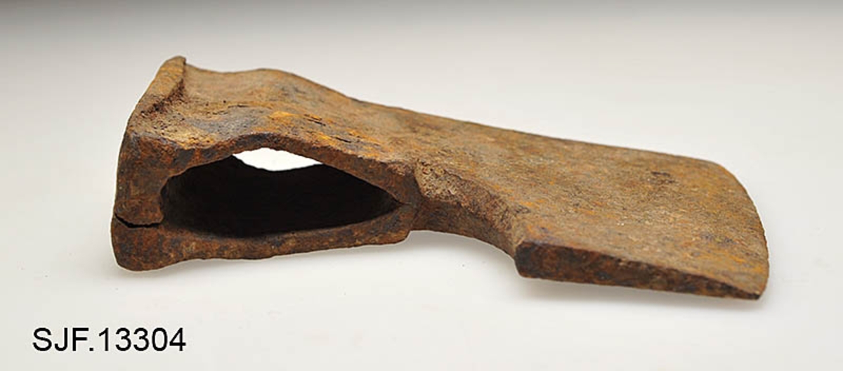 Økseblad uten skaft.  Redskapet er overført fra Borgarsyssel museum i Sarpsborg, dessverre uten proveniensinformasjon ut over at den skal være brukt i Østfold. 

Øksa er smidd, antakelig med innlagt stål i eggpartiet, men ettersom overflata er dekt av rust er det vanskelig å verifisere dette uten å foreta oppsliping.  Dette framstår som et forholdsvis tungt og bredt økseblad.  Med denne bladbredden har det neppe har vært beregnet på hogst, men det kan naturligvis ha vært brukt til barking, men også til ymse håndverksaktiviteter.  Den øvre delen (omkring øyet og nakken) er preget av slitasje.  Det nedenforliggende bladet er noe bredere.  Nakkedelen har opprinnelig vært flat og rektangulær, men den er brukt som hammer, noe som har ført til at godset er noe deformert og at det har dannet seg "skjegg" langs langsidene.  Øyet (skafthullet) har et dråpeformet tverrsnitt (cirka 5, 2 X 2, 6 centimeter). Godset mellom øyet og hammerflata på øksenakken er sprukket, noe som kan ha vært årsak til at redskapet ble kassert.  Eggdelen har betydelig større bredde enn nakkedelen. 
