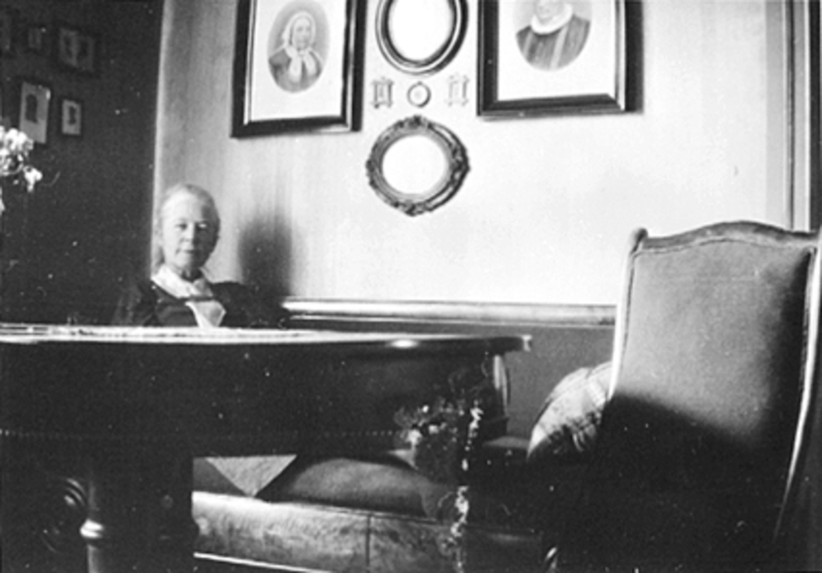 INTERIØR STUE, INGEBORG PETERSEN VED BORDET BILDER AV STABEL PÅ VEGGEN, FAGERVIK, ØSTREGATE 72