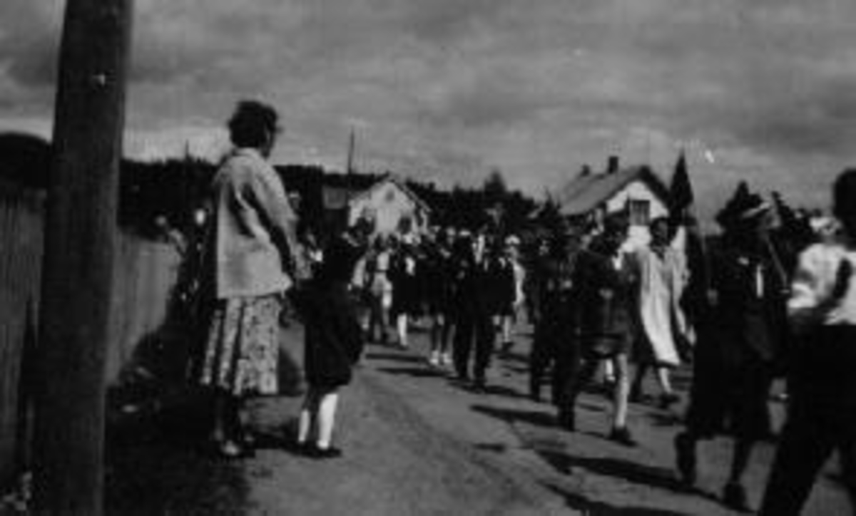 17 mai tog i Berger Langmoens veg, Brumunddal. Skolemusikken med fane. Politimann foran.