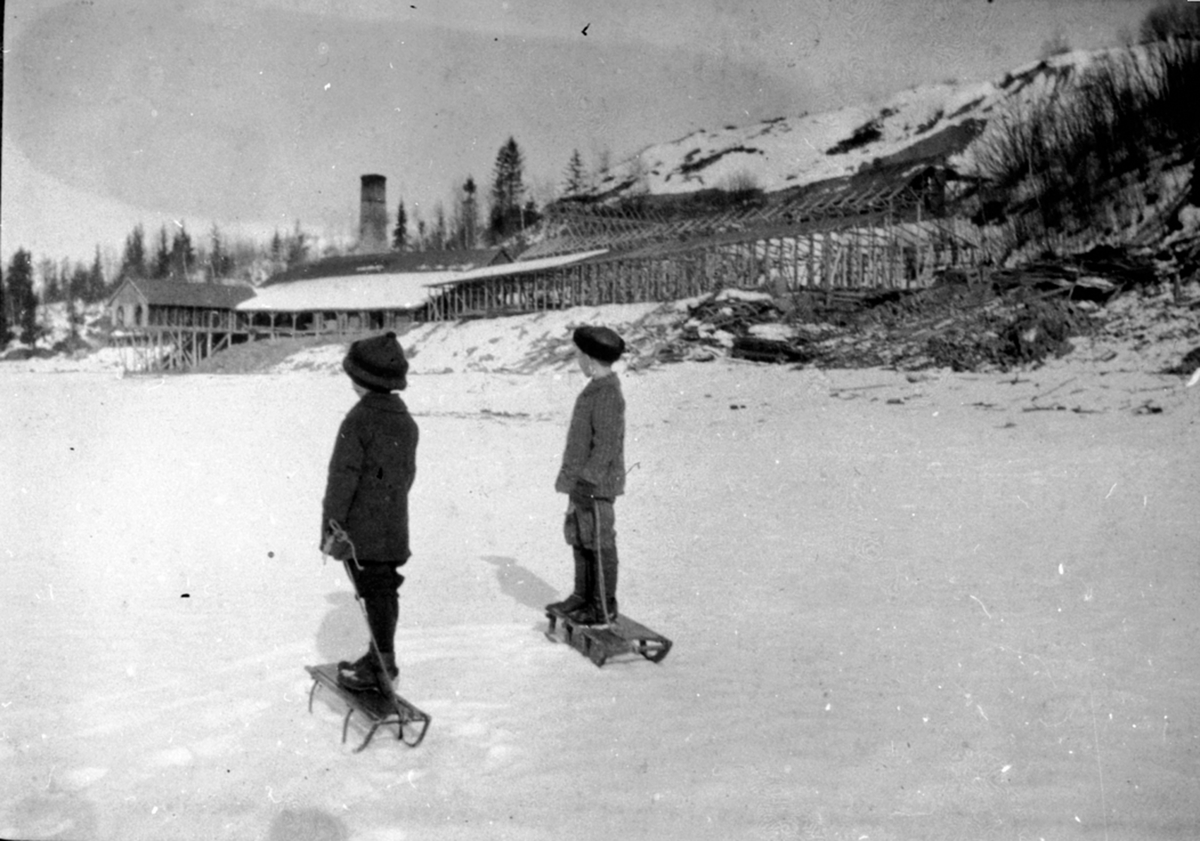 Sendstad teglverk sett fra Mjøsisen. 2 gutter med kjelker. Nes, Hedmark.