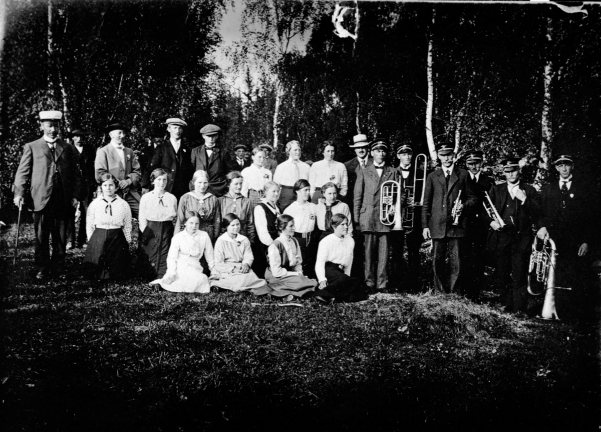 Nordaasen musikforening med instrumenter og Hemmakoret. Musikere i Nordaasen er fra høyre, Mathias Berger,Julius Harilstad, Karinus Bakkerud, Petter Mausethagen, Johan Glorud og Trygve Sortungstad. Dette bildet skal være tatt rundt St.hans 1915.