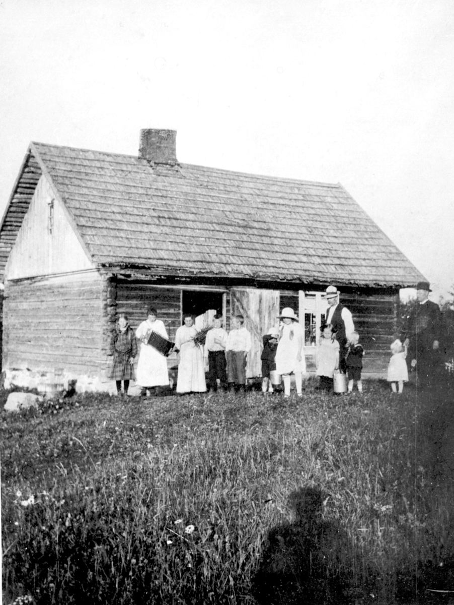 Husmannsplassen Svartbækken/Høystad, Helgøya. Stor gruppe barn og voksne foran huset.