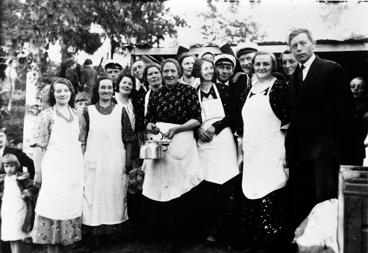 Kantinedamene på musikk- og sangerstevnet på Kjevlehaugen, Næroset. Damene fra venstre er Klara Kjelsmoen (G. Hagen), Bergine Kjelsmoen, Alma Bårdseth, Anna Bratberg, Berthe Sagen med kaffekjel, Klara Kjelvold, Elvsvebakken, Magnhild Skar. Ringsaker 1936.