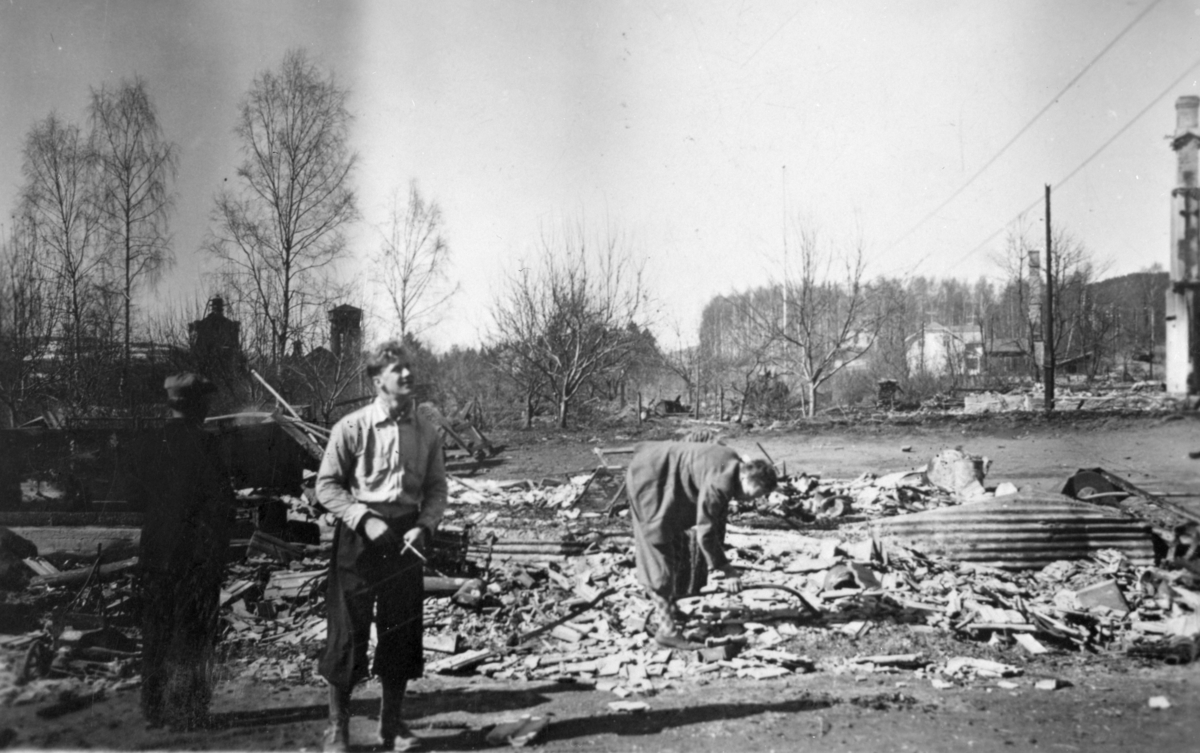 Branntomtene ved Kilde skole, juni 1940. Fire brannruiner, den borterste hos kjøpmann Haugen. Midt i bildet ser vi en person med vedsag., I forgrunnen Ahlsens hus og anleggene og disponentboligen til Cellulosen.  Husene ble skutt i brann av tyske soldater i aprildagene 1940. 2. verdenskrig. 