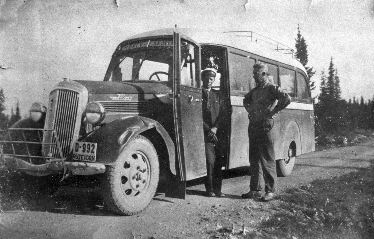 Buss,  med reg. nr. D-992, rutevogn Moelv-Skolla. Gunnar Grøtlien kjørte i mange år fjellruta Moelv-Skolla om Bergundhaugen og Ljøsheim.. Her er en av bussene avbildet ved Storstilen, med sjåføren Lars Ulven sammen med Bernhard Pedersen. Bildet er fra 1936-37. Bussen er en Reo Speed Wagon med plass til 24 personer. Det var stor trafikk innover fjellet på den tiden, før personbilene var noe særlig utbredt.