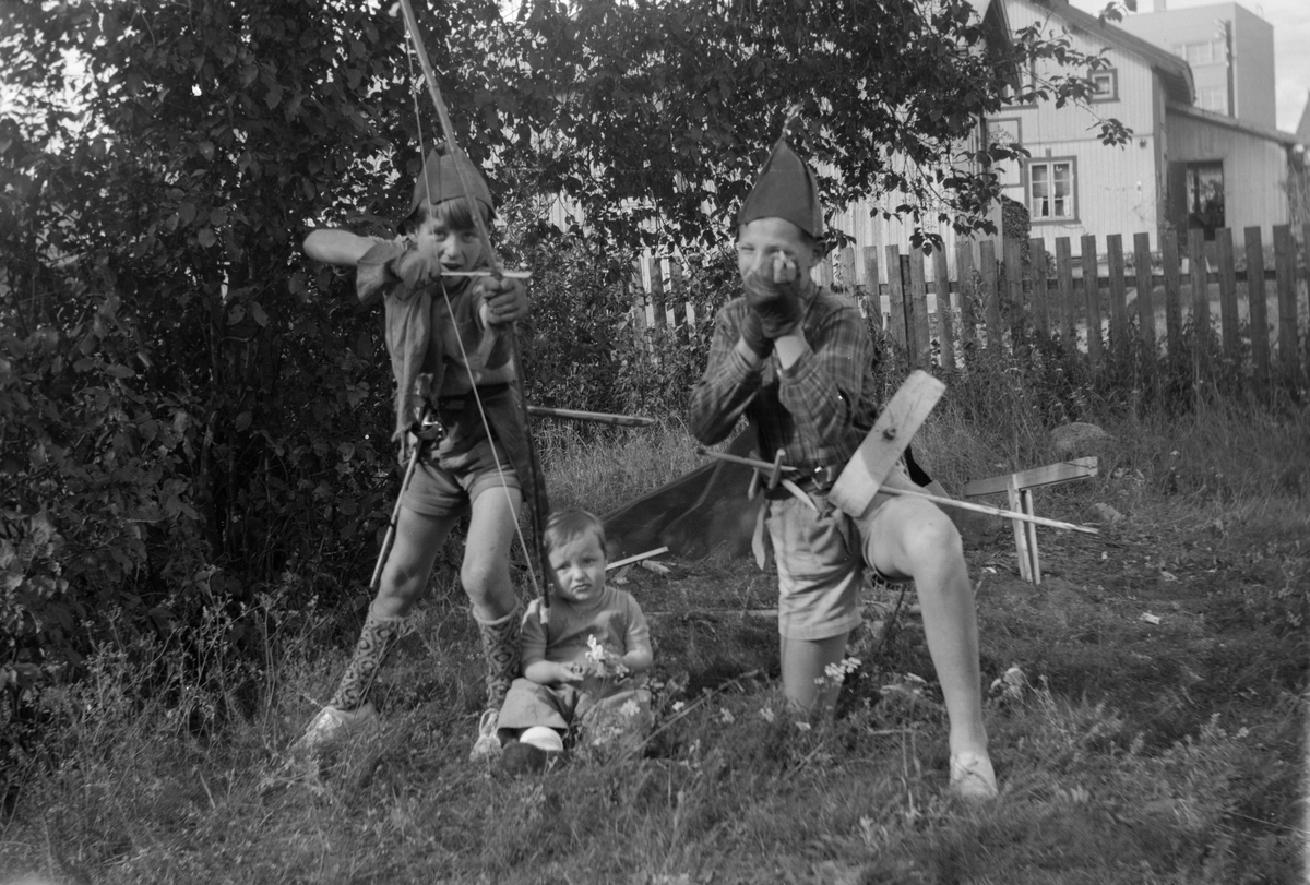 Mordal i Nygata 21 i Brumunddal. Barn. Barnelek. Lek i Husebyenga fra v. Svein-Erik Mordal f. 1941, Vilde Kari Mordal f. 1951 og Arne Dag Mathisen. I bakgrunnen Hansens bolighus og Gudahl-bygget.