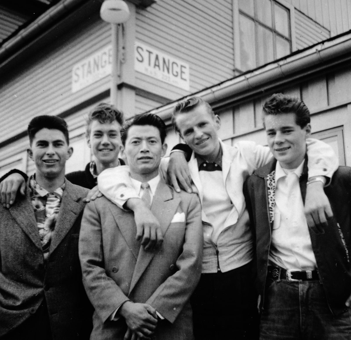 Landkrabbene f. v Hans Nyland og Jens Sørholte og uteseilerne Che Quan Fah, Harald Løken og Kaare Moen venter på toget fra Hamar, som skal ta Che og Harald tilbake til Oslo, etter en spontan avmønstring i Stange. Stange jernbanestasjon 19. juni 1958. 