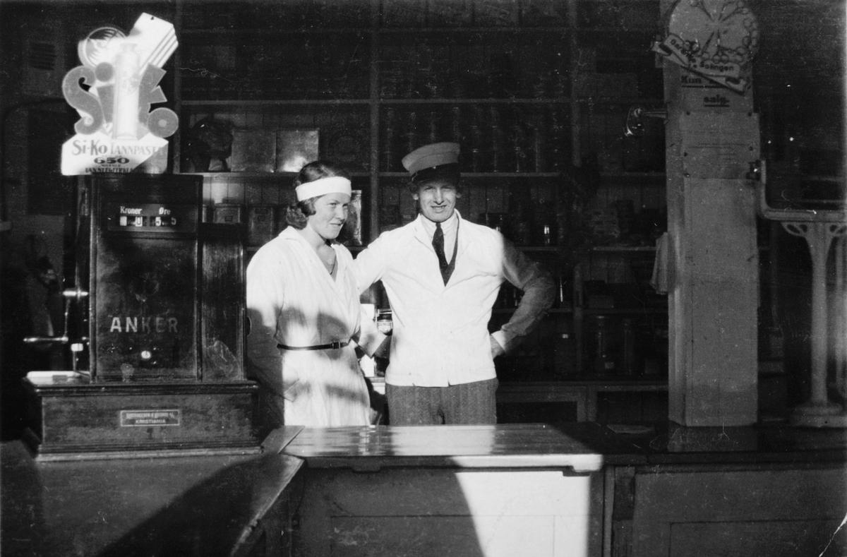 Butikken til Bekkelaget kooperative selskap, butikkinteriør. T. v Inger Johansen og ekspeditør Martin Martinsen (Tømte) f. 29. 11. 1911, 1930-tallet. Reklame Siko tannpasta, Anker kassaapparat. 