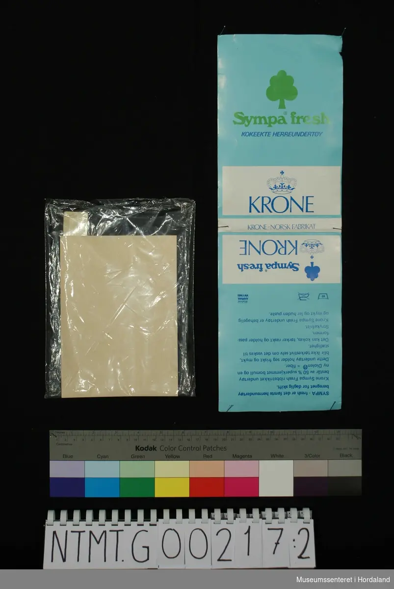 Kvit Krone singlet utan ermer. Plagget har merkelappar i tekstil med Krone-merket og ein kløver for varemerket Sympa fresh - eit blandingsmateriale i superkjemma bomull og Diolen (polyester). Ifølgje reklamen er plagget strykefritt, tåler kokevask og held seg mjukg og med god passform.