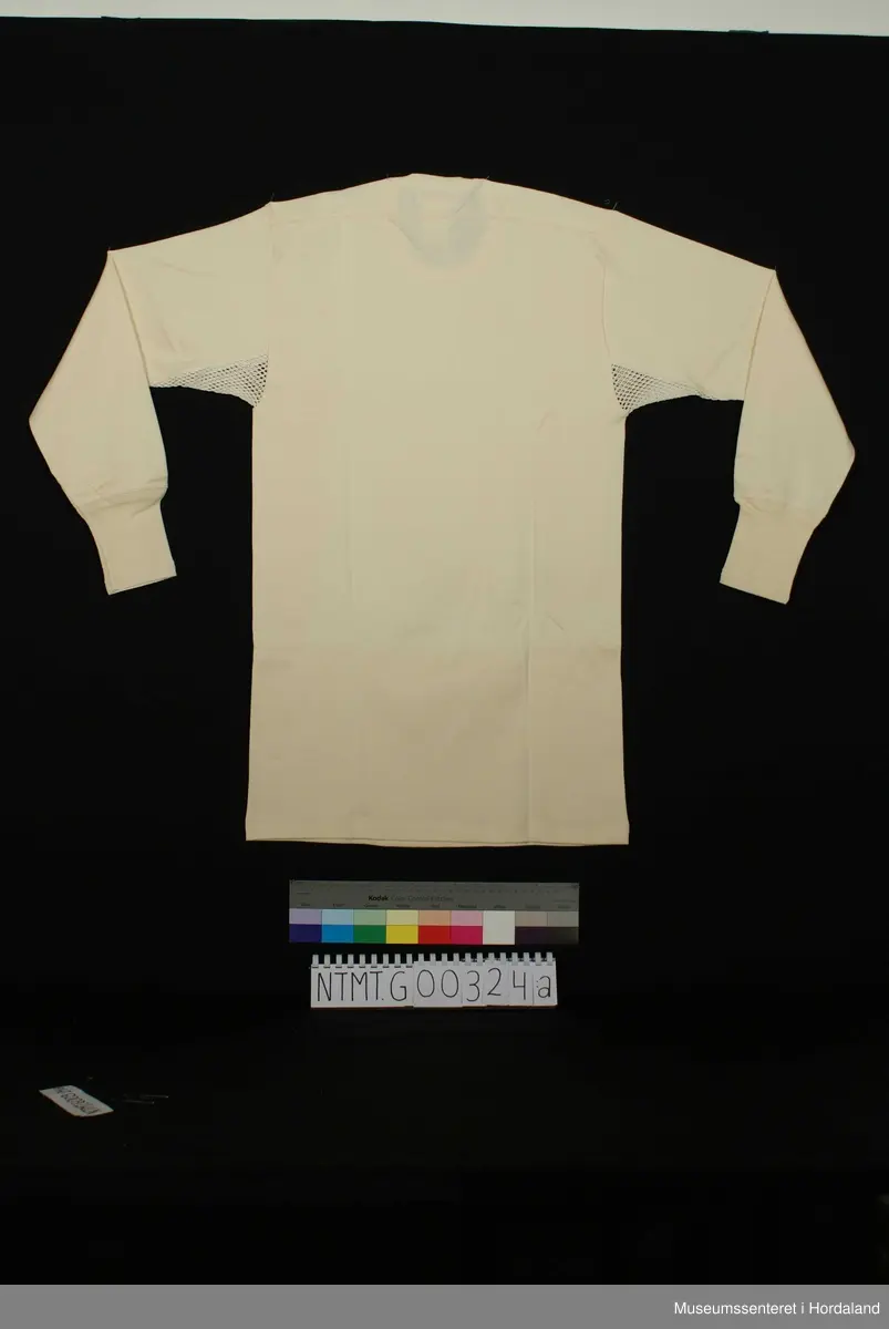 Rund hals, lange ermer med brotavslutning, kile under ermer, skulderstykker.