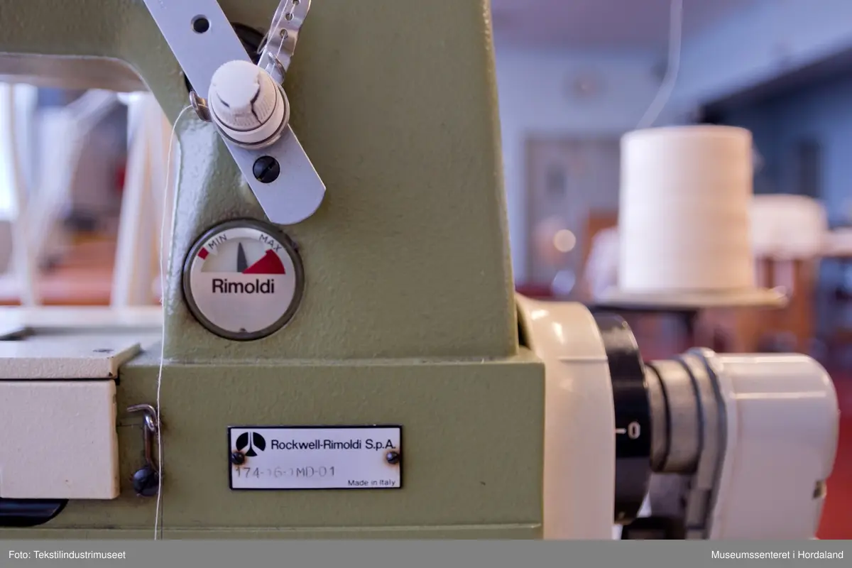 Rimoldi-symaskin montert på lite bord med pedalar og motor under bordet, og stativ til to trådsneller og trådførarar ved sidan av maskina. Strømbrytar er plassert under bordet.

Motor: Etka Variostop
Typ: VD 12
Nr. 08315789
3~Mot (triangel)Y 220/380 V
2,6 / 1,5 A     550 W
2800 / 3400 1/min
...
Made in Western Germany