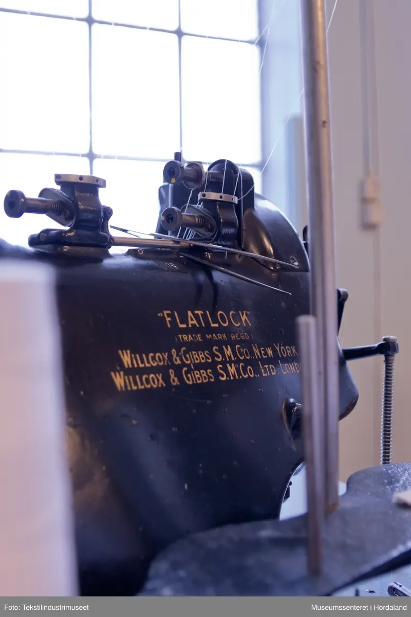 Flatlock-symaskin i svartmåla støypejern og med halvautomatisk oljing. Maskina er montert på eit Juc-bord og har Singer-motor (truleg ikkje original).

Motor: Singer alternating current electric transmitter. No. K 692357 R
Volts: 210-230.