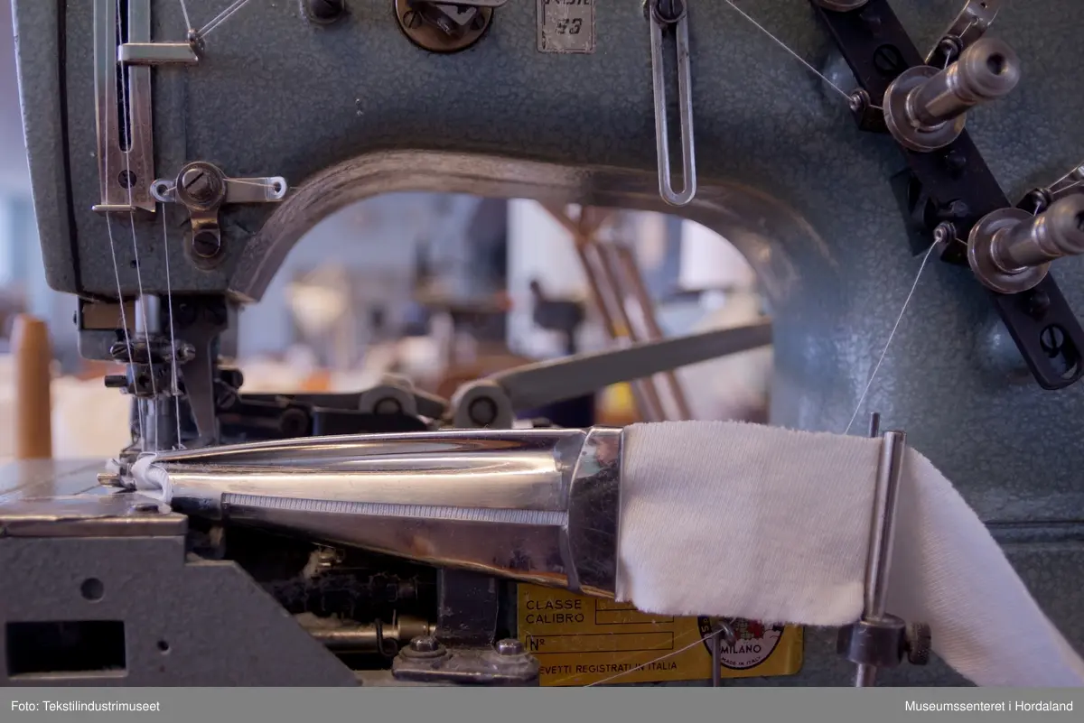 Rimoldi-symaskin som syr kantband til klede av strikka tekstilar (trikotasje). Ein kan sy med to og tre nåler og ein dekktråd. Ein tråd under ("looper"). Ein brukar band som er kutta til på ei anna maskin og rulla opp, plasserer ein enden av bandet i eit bandapparat i metall. Det blir så mata gjennom dette og sydd. 
Maskina er av klasse 1363 - 25.