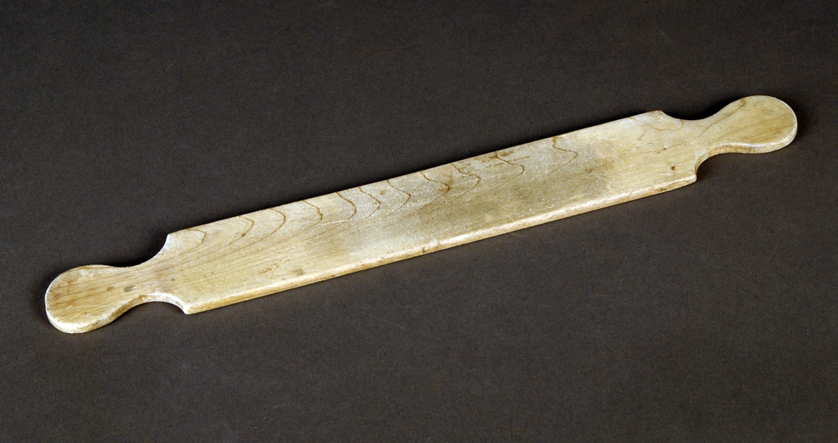 Utstyr til pilletrilling i to deler. En rektangulær metallplate med riller som er skrudd fast i en tilpasset treramme med flate, knoppformete ender. En tynn, flat treplate med lignende knoppformete ender følger med.