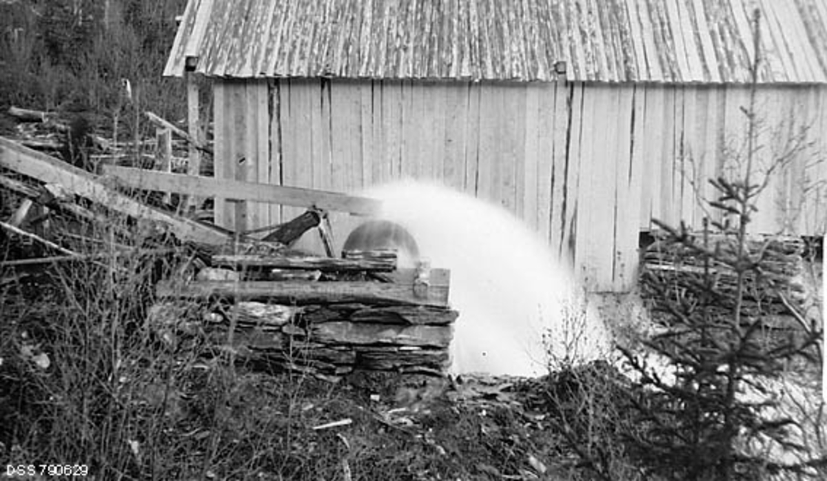 Eksteriør fra vanndrevet gårdssag i Skardmodalen i Hattfjelldal på Helgeland, fotografert i 1913. Fotografiet er tatt mot vasshjulet, som drev mekanikken inne i det bordkledde saghuset i bakgrunnen. Vi ser et hurtigroterende underfallshjul som settes i rask rotasjon ved at en vannstrøm fra ei forholdsvis bratt renne ledes mot skovlene på undersida av hjulet.