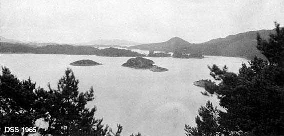 Utsikt fra Lysekloster-komplekset.  Fotografiet er tatt fra en bergskrent eller åskam over et fjordlandskap med holmer og øyer.  Landskapet er dels bevokst med furuskog. 