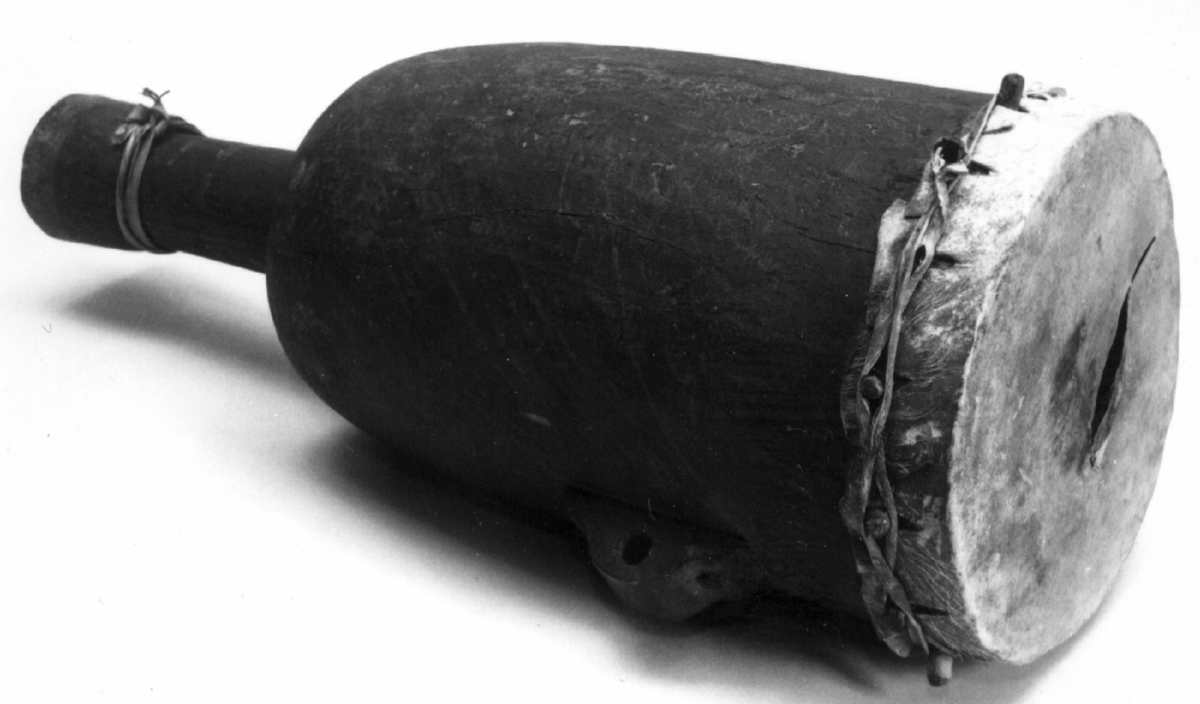 Vaseformet ståtromme av brunmalt tre. Enfells.
Lyst skinn, delvis med hårene på. Skinnet er naglet fast med trenagler, dertil forsterket ved en sirkulær skinnsnor, festet til en jernhempe.
Nedre ende er skåret som en sokkel. En brunmalt trehank er spikret   med 2 kraftige jernskruer på trommens ene side.