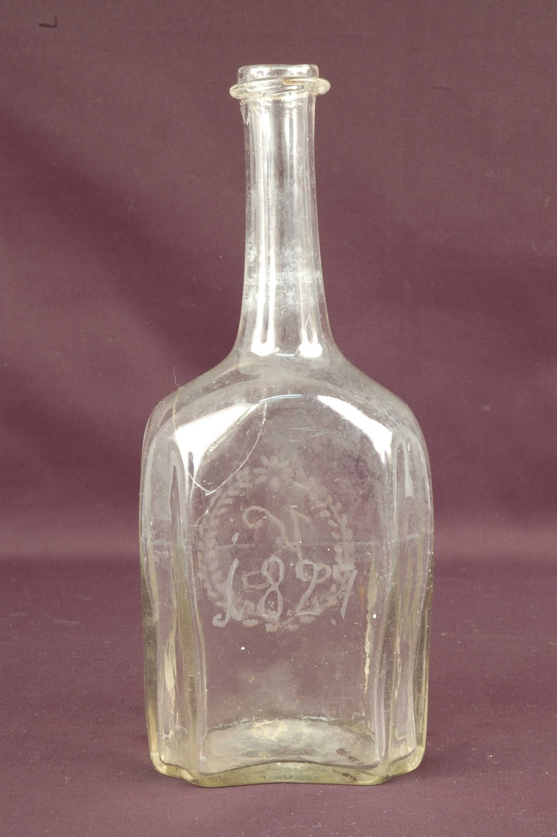 Åttekantet brennevinsflaske med lang tut. Gravert tekst på blankt glass.