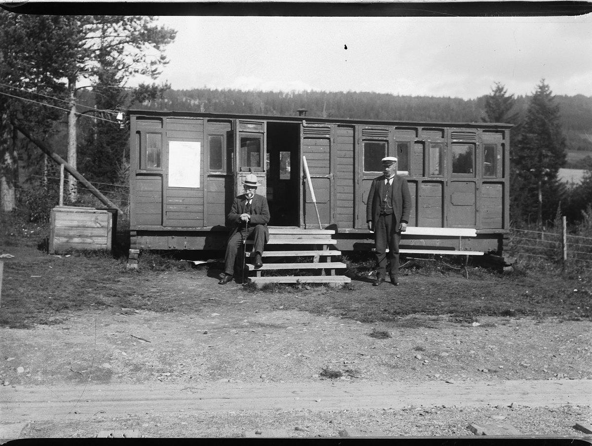 Ringsaker, Rud stoppested anlagt 15.11.1915, Rudshøgda stasjon. En gammel jernbanevogn ble i begynnelsen brukt som stasjonsbygning. Kjøpmann og gårdbruker Jacob A. Rud (1866-1953) var ekspeditør for post og jernbane inntil Christian Nordby ble stasjonsmester i 1918 til 1925, kjøpmann Ole Skaraasen (1856-1922) til høyre, stasjonsmesteren var opplært av Johs. Ensby som var telegrafist ved Ringsaker stasjon,