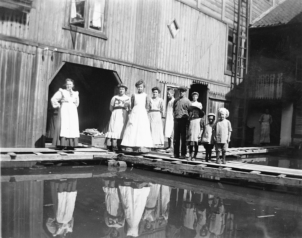 Hamar, Strandgata 15, baker og konditori O. Johannessen (Bager & Conditor), etablert i1902, drift fram til 1958, sønnen bakermester Johs. Johannessen tok over etter faren Olaus Johannessen i 1916, bakeri i bakgården, Mjøsflommen i 1927, gruppe ansatte og familie på oppbygde gangbroer, Bakermesterfrue Lovise Johannessen til venstre,