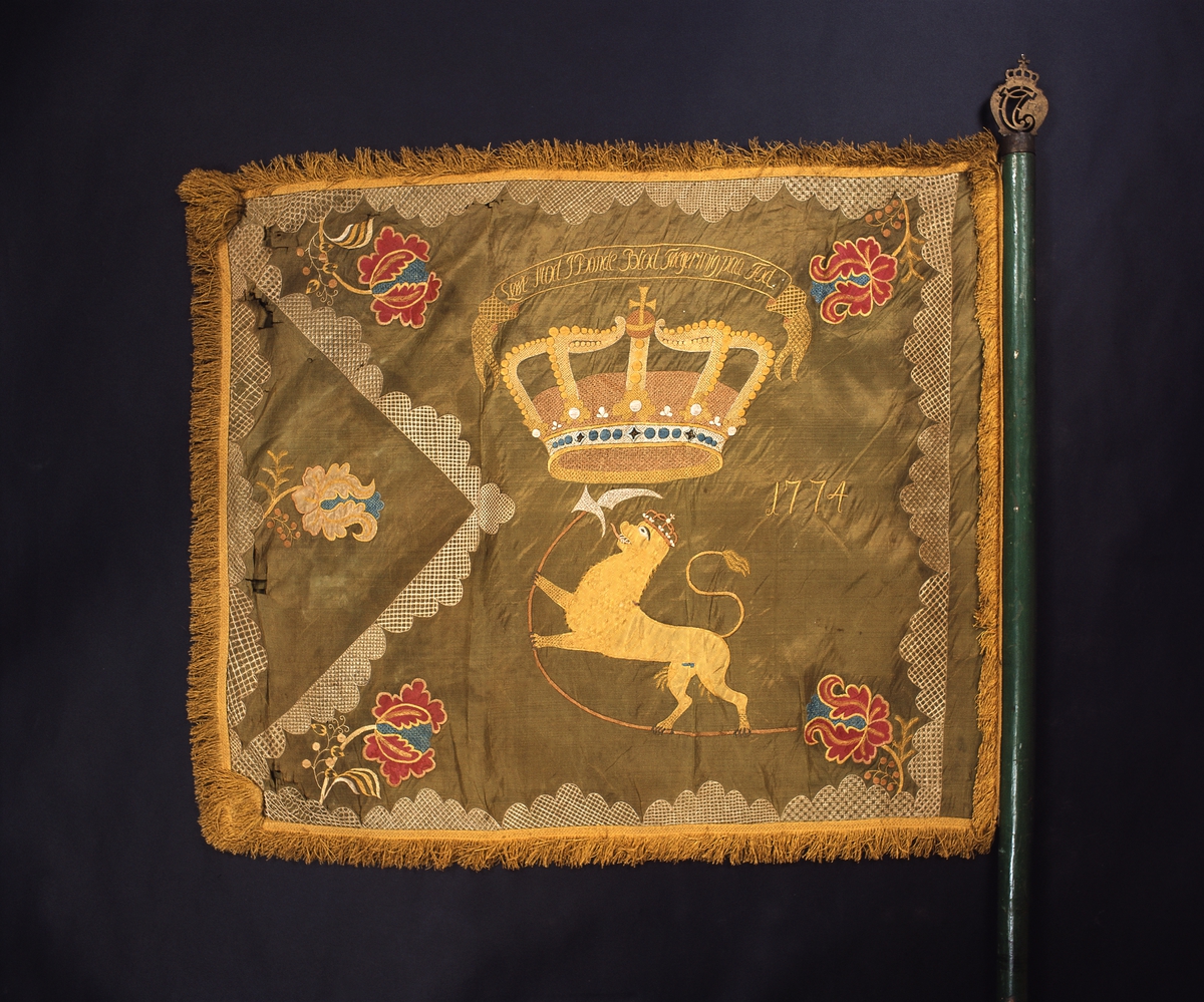 Fane. Bygdefane fra Stange. Forsiden av fane fra 1774 fra Det Stangerske Bondekompani. Over kronen står innrammet "Løve Mod i Bonde Blod Følger mig på Fod" OF.7593.