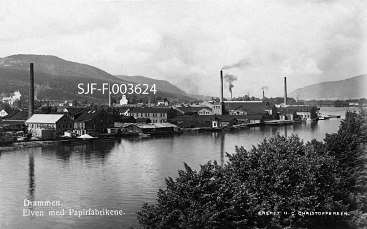 Papirfabrikkene på vestsida av Drammenselva.  Fotografiet er antakelig tatt fra bybruas bruhode på østre side mot industriområdet, som også ble kalt for Grønland.  Fabrikkene ligger på rekke og rad, med produksjonslokaler i teglstein, alle med en gavl mot elva og en mot den bakenforliggende jernbanen, som vi ikke ser på dette fotografiet.  Flere av bedriftene hadde høye, sylindriske skorsteinspiper.  På en bakkekam bakenfor fabrikkene ser vi ei kvitmalt kirke, antakelig Strømsgodset kirke (Sundhaugen).  I bakgrunnen ruver skogkledde åser mot horisonten, på begge sider av vassdraget. 

I 2018 fikk Norsk skogmuseum følgende kommentar til dette fotografiet fra Egil Øygard:

«Nå er det bare én papirfabrikk igjen, Sunland og Eiker Papirfabrikk. Området har blitt totaloppusset med boliger, restauranter og kontorer og blir i dagligtale kalt for Union Brygge.»