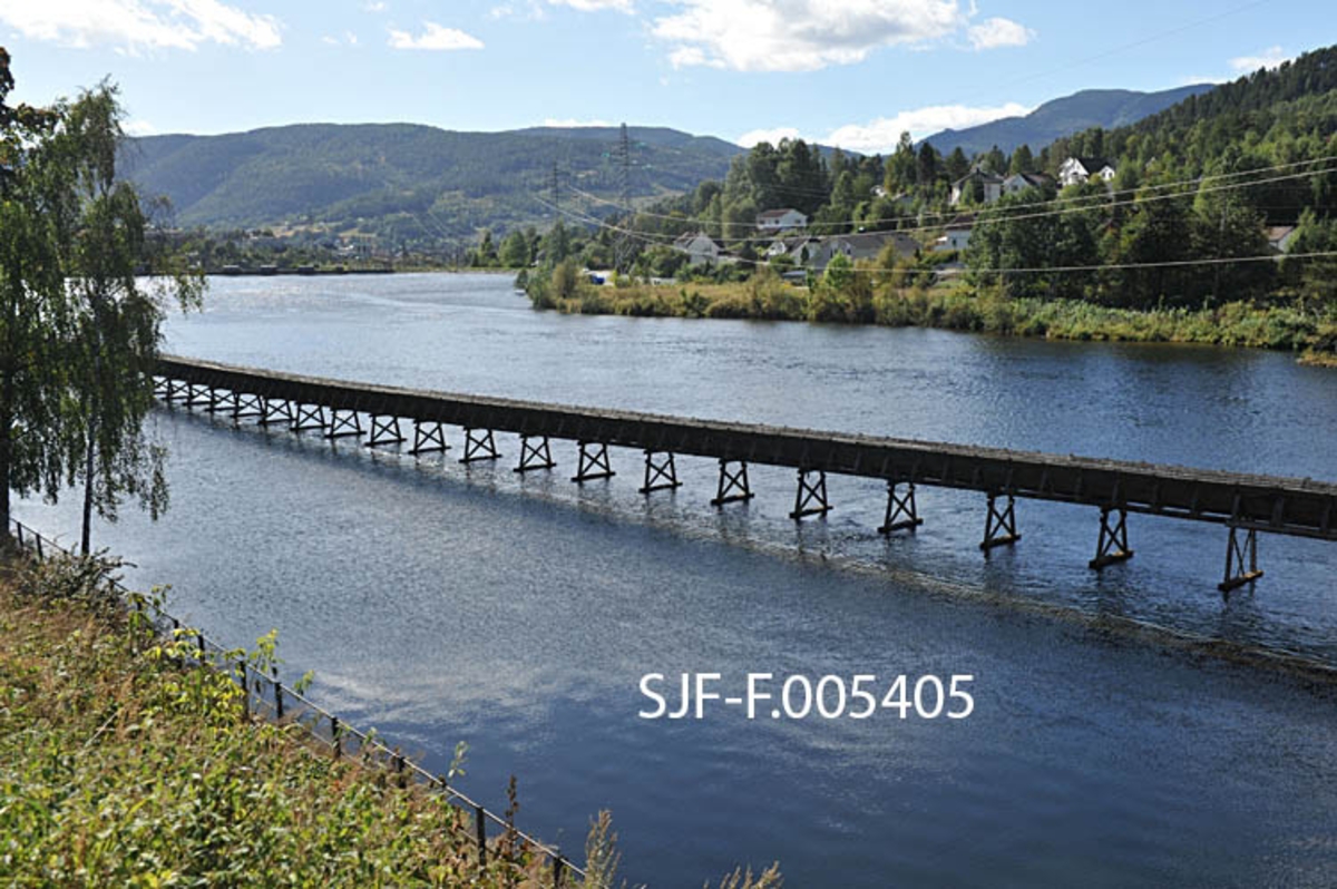 Tømmerrenna på Notodden, fotografert der den går langs den østre delen av Sagafossdammen.  På innersida av renna, under vannflata, skimtes noe som kan se ut til å være en gammel skådam. 

De mange kraftverksprosjektene i Tinne/Tinnelva tidlig på 1900-tallet gjorde det nødvendig å bygge tømmerrenner som skulle ta tømmeret forbi kraftverksdammene.  I 1920-åra ble det bygd ei renne fra Lienfossdammen, forbi Sagafoss og Tinnfoss.  Denne renna ble 1 863 meter lang.  Den nedre delen av den renna står på søyler i Årlifossdammen på dette fotografiet.  Fløtinga på Tinnsjøen ovenfor opphørte i 1970.  Seinere har det bare unntaksvis gått tømmer i renna, siste gang i 1992.  På denne tida innså man at renna var et viktig kulturminne.  I midten av 1990-åra ble det igangsatt restaureringstiltak i samarbeid med kommunale og regionale verneinteresser og Skiensvassdragets Fellesfløtningsforening, som fridde seg fra videre ansvar ved å skyte inn et beløp som tilsvarte stipulerte rivingskostnader.  I 2012-13 vurderer Riksantikvaren fredning av tømmerrenna på Notodden. 