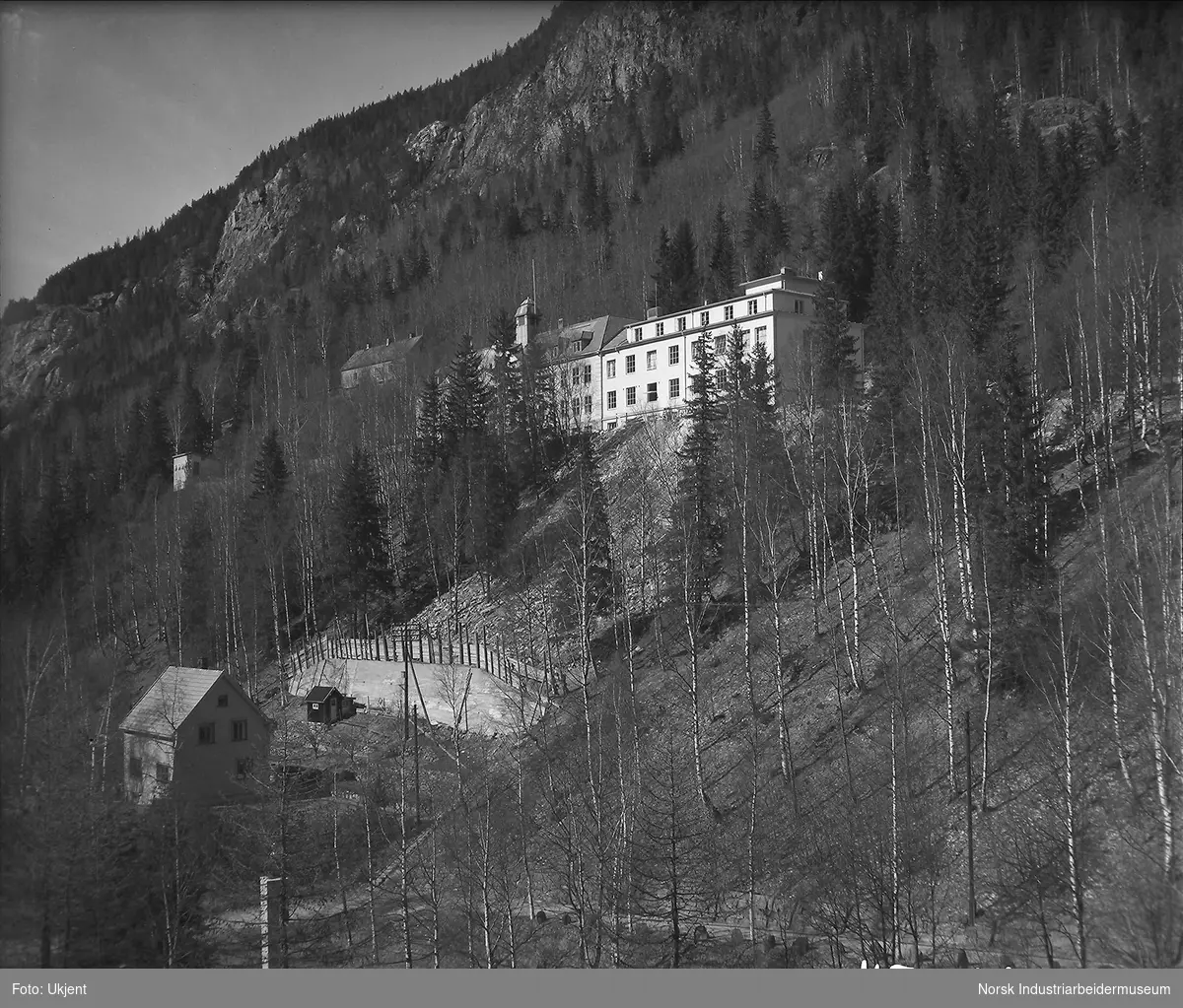 Rjukan sykehus og lasarettet, foto tatt fra kirketårnet. Bolighus vest for sykehusbakken og mur opp mot sykehuset i lia bak huset.