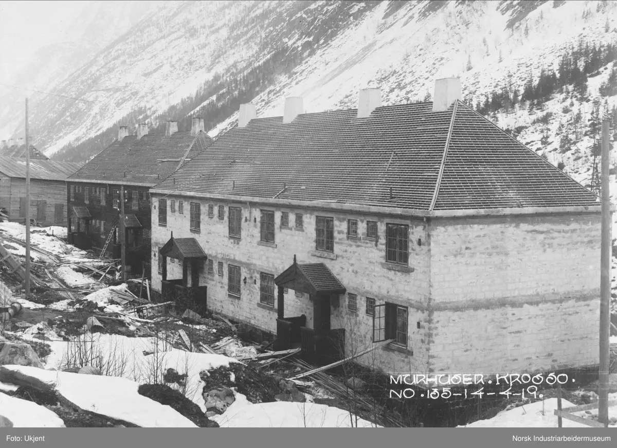Murhusbebyggelsen på Krosso under oppføring. To bygninger ferdig reist med inngangsparti, dører og vinduer. Taket har fått sløyfer og lekter, men ikke takstein. Fire piper på taket.