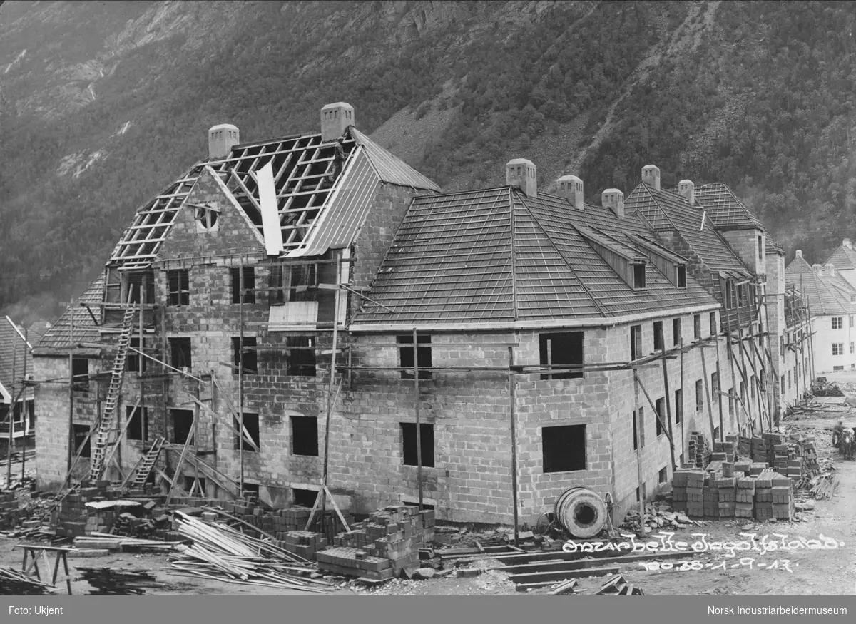 Murbebyggelsen Sing Sing, murbelte på Ingolfsland, under bygging. Øvre Sing Sings nordre del. Arbeider tetter taket med takbord, papp, lekter og sløyfer. Stabler med murstein stående rundt bygget. Stige lent opp langs veggen.