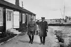 Två manliga högre officerare går framför en huslänga vid en hamn.