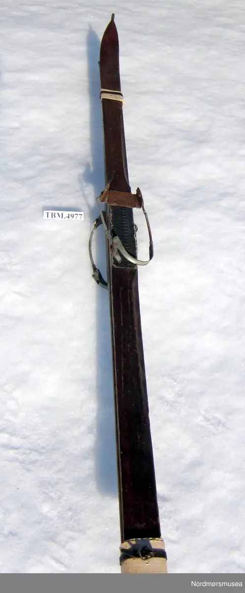 Ski med opphøgd rygg og Huidtfeldbindingar med vaier med spenne. Ei renne under skia. Beisa og lakkert på oversida.