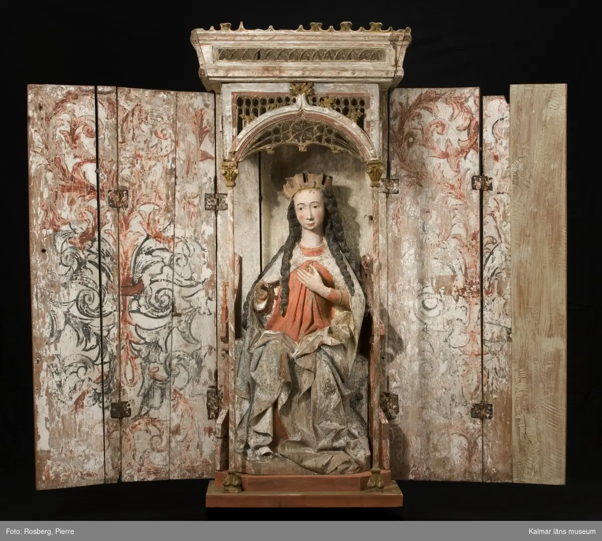 KLM 8048. Altarskåp, madonnaskåp. Av ek med sittande Madonna. Baldakin med masverk och ett krönande överstycke med masverk, krönet är snedställt. Baldakinens masverk döljs när dörrarna är stängda. Baldakinen bärs upp av två kolonner. Skåpet har dubbla vikbara dörrar. Det vänstra dörrparet består av fyra plankor, sinsemellan sammansatta två och två med dymlingar i fogarna. Det högra dörrparet består av i den inre dörren endast av en planka, den yttre har en ny planka limmad till den äldre delen. Skåpets bakstycke är sammansatt av två plankor. Skåpets plankor är varierande i bredd. Bottenplatta och sockel för stolen är nytillverkade. Barnet och Marias högra arm saknas, liksom kronans blad och några av krönets taggar. Dörrarnas insidor med målad bladornamentik, akantusornamentik, i rött, svart, grått, vitt. Marias kjortels nuvarande bemålning är rödbrun, under denna syns den ursprungliga kraftigt röda färgen, man kan även ana schablonmönster, den ursprungliga färgen är bevarad i stor omfattning. Rester av blått i foder. Mantelns nuvarande bemålning är ljust blå. Datering: 1400-tal. Nuvarande bemålning 1600-tal eller tidigt 1700-tal.