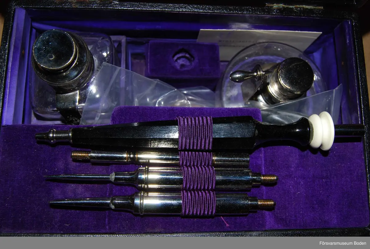 Etui klätt med konstläder på utsidan och sammet på insidan, innehållande två bränslebehållare med gummiboll och slangar samt handtag med platinamunstycken. Bruksanvisning medföljer.
