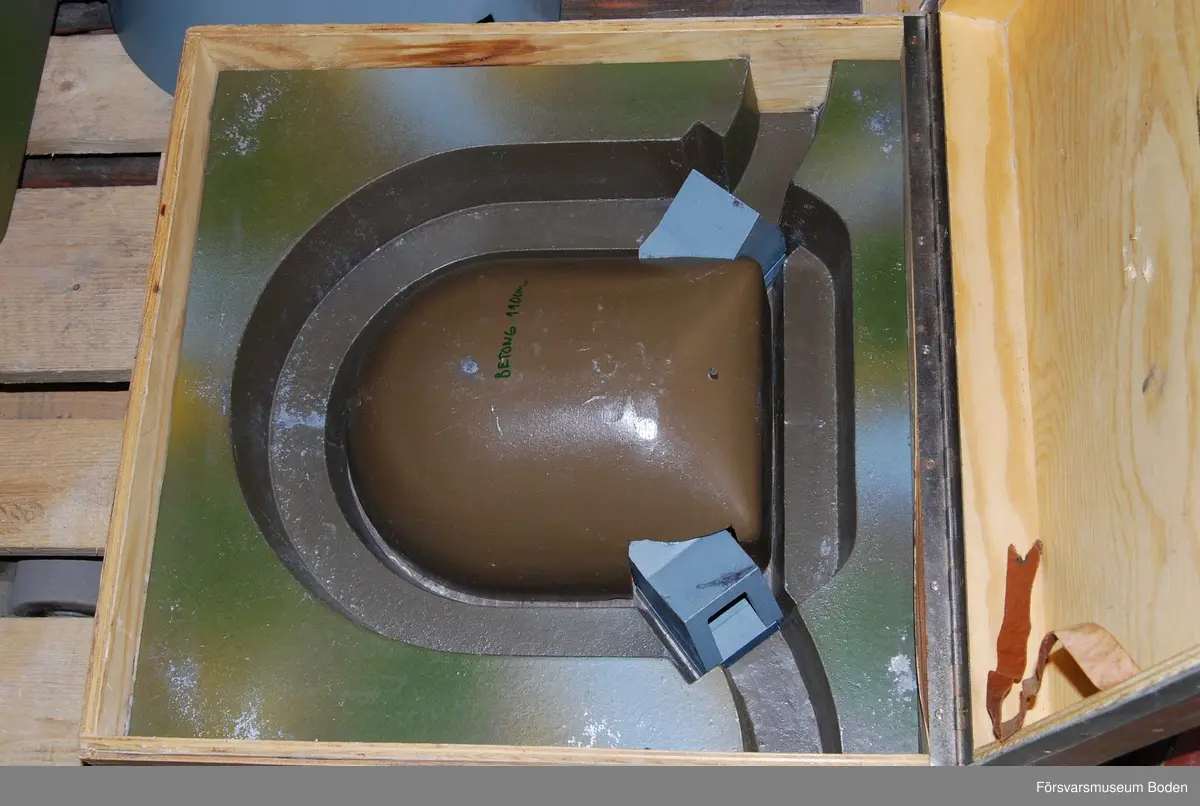 Modell i skala 1/25 av kupol, uppbyggd i flera avlyftbara lager av gjuten aluminiumlegering som målats. Placerad i trälåda med bärhandtag (defekt) och med gummifötter för att kunna ställas på högkant. Lagrens typ skrivna med tusch, vilket verkar ha gjorts i efterhand.