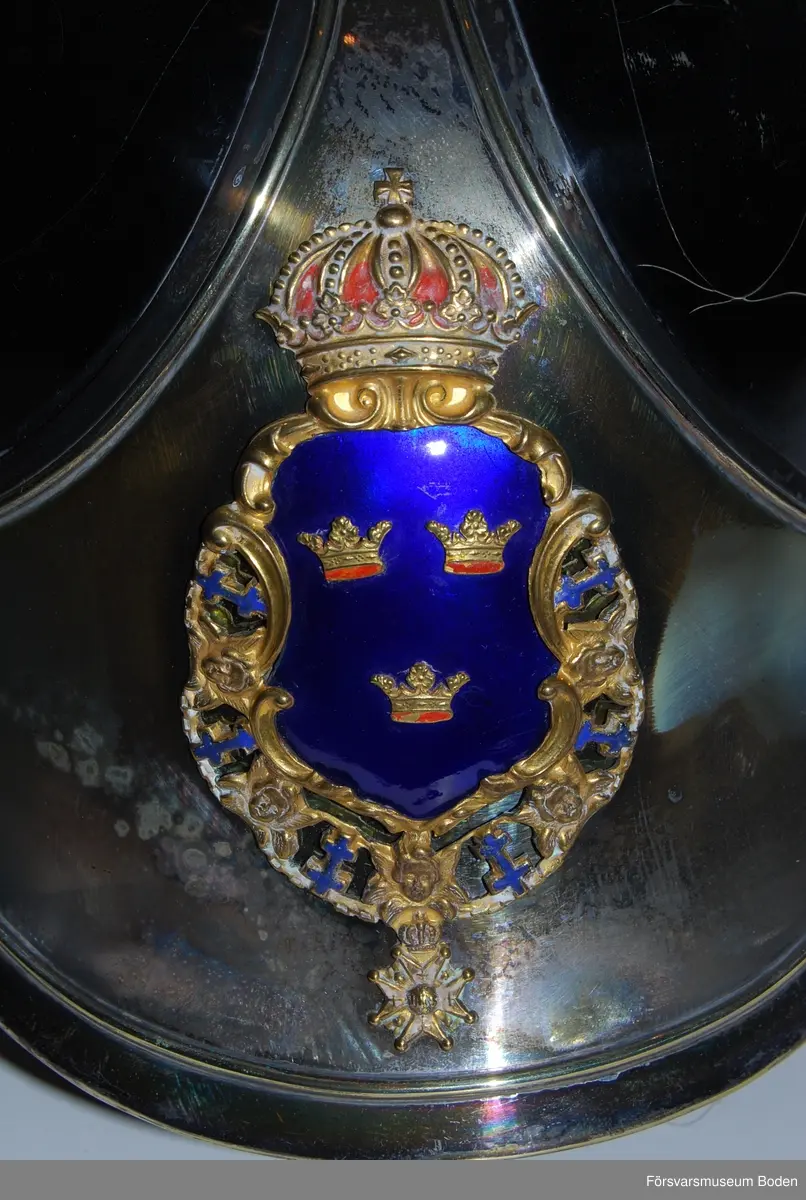 Av svartlackerat läder med försilvrad framplåt och bakskena. Förgylld lagerkrans runt kullen.  Upptill skruvfäste för plym m/1887 av vitt tagel (vid stor paraddräkt) eller pik. Förgylld fjällmönstrad hakrem med lejonmaskaroner. Gul sidenkokard under hakremsknappen på höger sida. Framtill förgylld vapenplåt med blå emalj.
