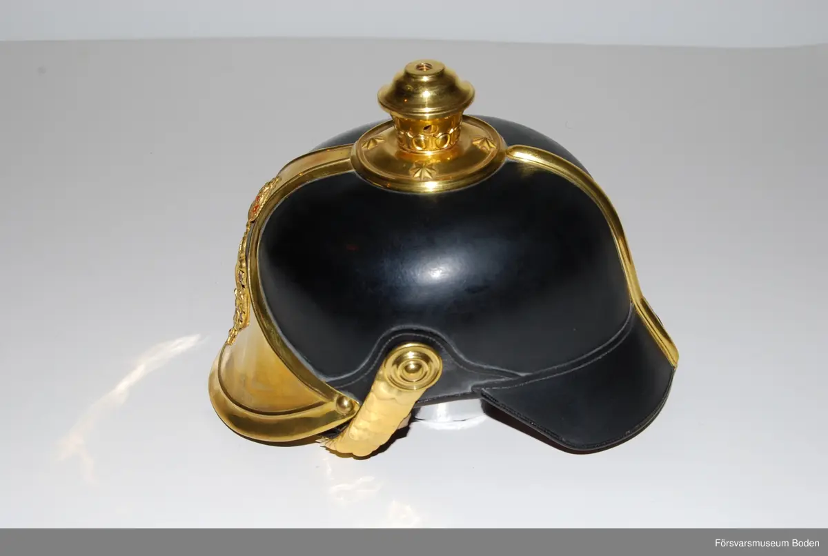 Svartlackerat läder med förgyllda beslag, framplåt, bakskena och hakrem. Förgyllt mössmärke med blå emalj. Gul sidenkokard under högra hakremsknappen. Med plym m/1885 av svart tagel, vilken användes vid stor paraddräkt. Pik medföljer ej.