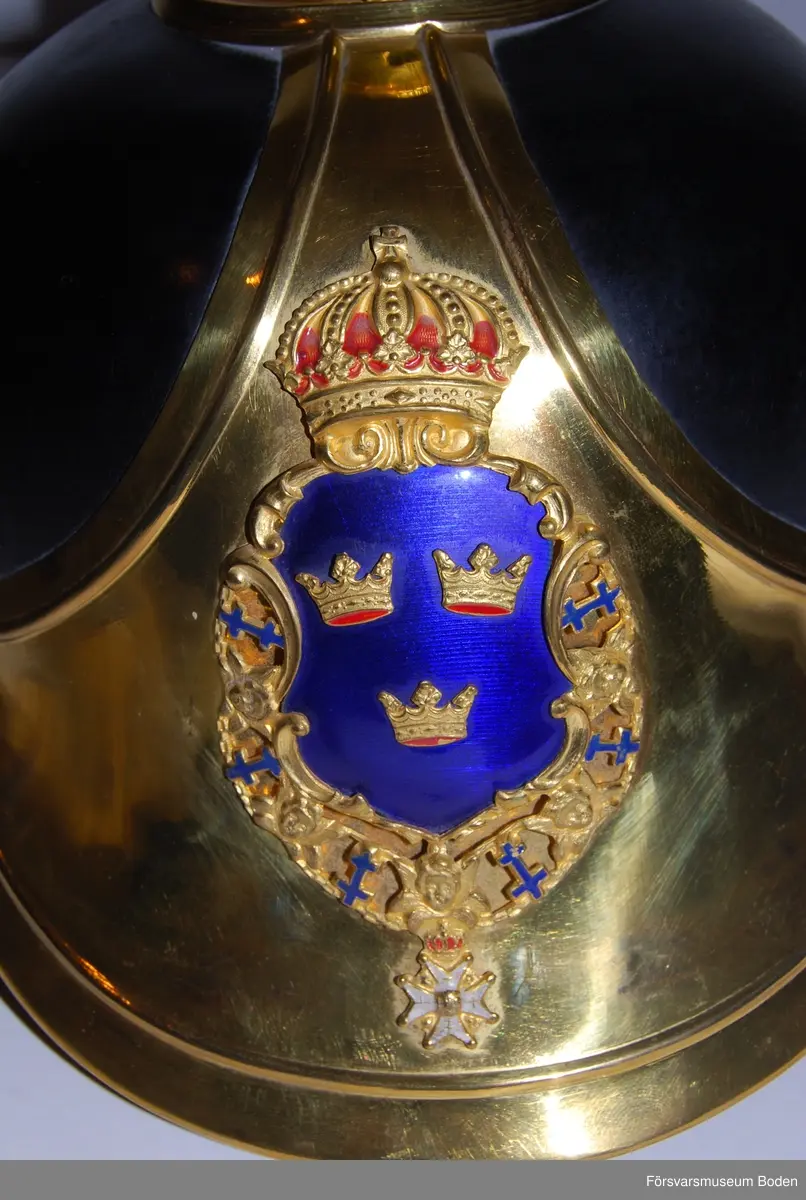 Svartlackerat läder med förgyllda beslag, framplåt, bakskena och hakrem. Förgyllt mössmärke med blå emalj. Gul sidenkokard under högra hakremsknappen. Med plym m/1885 av svart tagel, vilken användes vid stor paraddräkt. Pik medföljer ej.