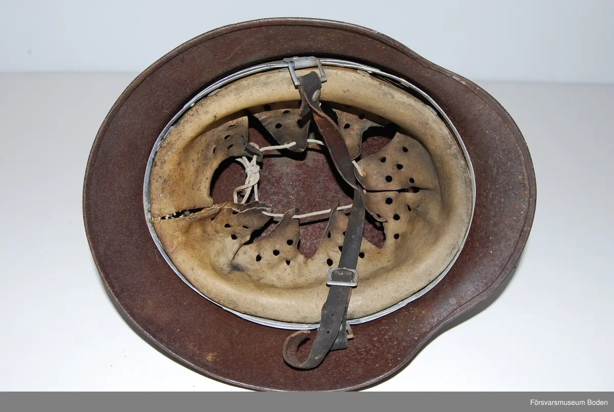 Kanten omvikt mot insidan. Inredning med aluminiumband, stämplat 1938. Rester av grön färg på insidan. Dekaler på båda sidor, varav endast rostkonturerna syns på den vänstra sidan. Storlek 59