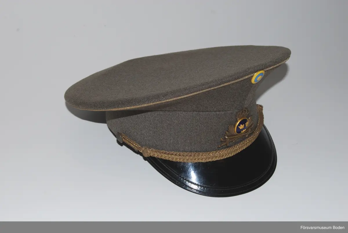 Gråbrungrönt ylletyg med mössmärke m/1939 i brons och blå emalj. Överst nationalitetesmärke m/1941. Mössrem bestående av flätad bred träns i bronsfärg för regementsofficerare, fäst på sidorna med regementets knapp modell mindre.