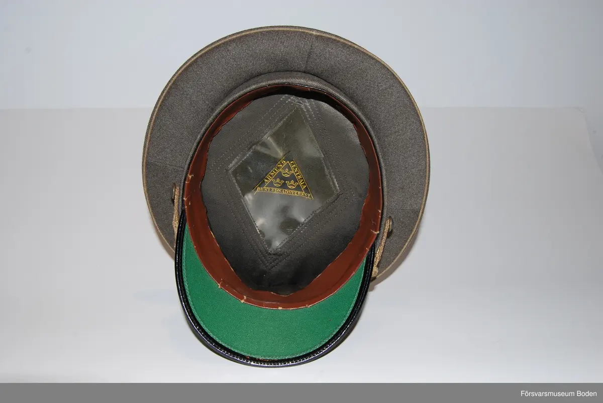 Gråbrungrönt ylletyg med mössmärke m/1939 i brons och blå emalj. Överst nationalitetesmärke m/1941. Mössrem bestående av flätad bred träns i bronsfärg för regementsofficerare, fäst på sidorna med regementets knapp modell mindre.